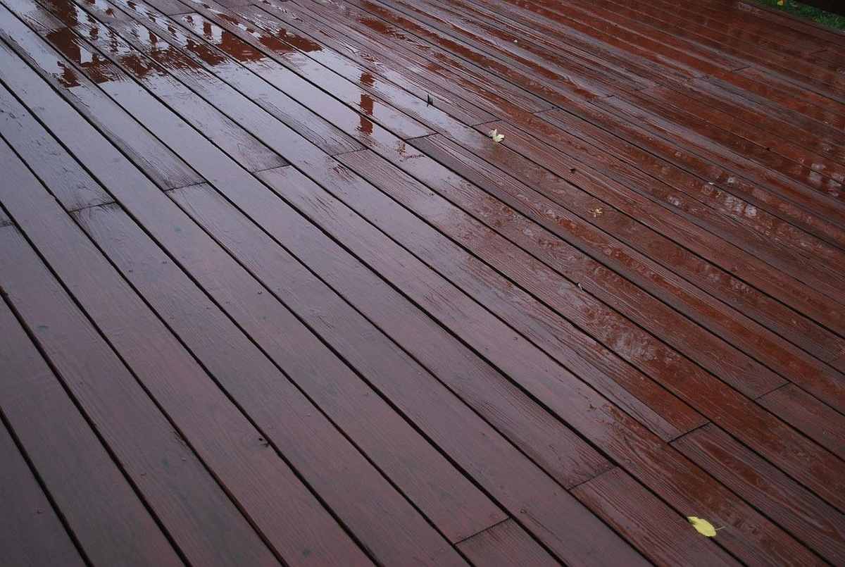 Plancher en bois mouillé reflète la pluie, quelques feuilles jaunes
